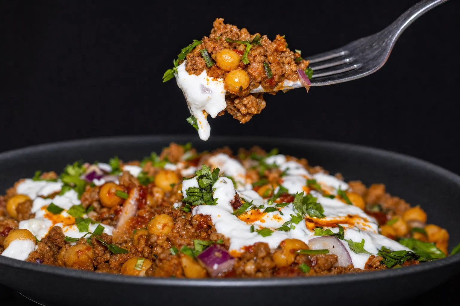 Nahaufnahme einer Gabel, die einen Bissen gewürztes Hackfleisch mit Kichererbsen und Joghurt hebt.