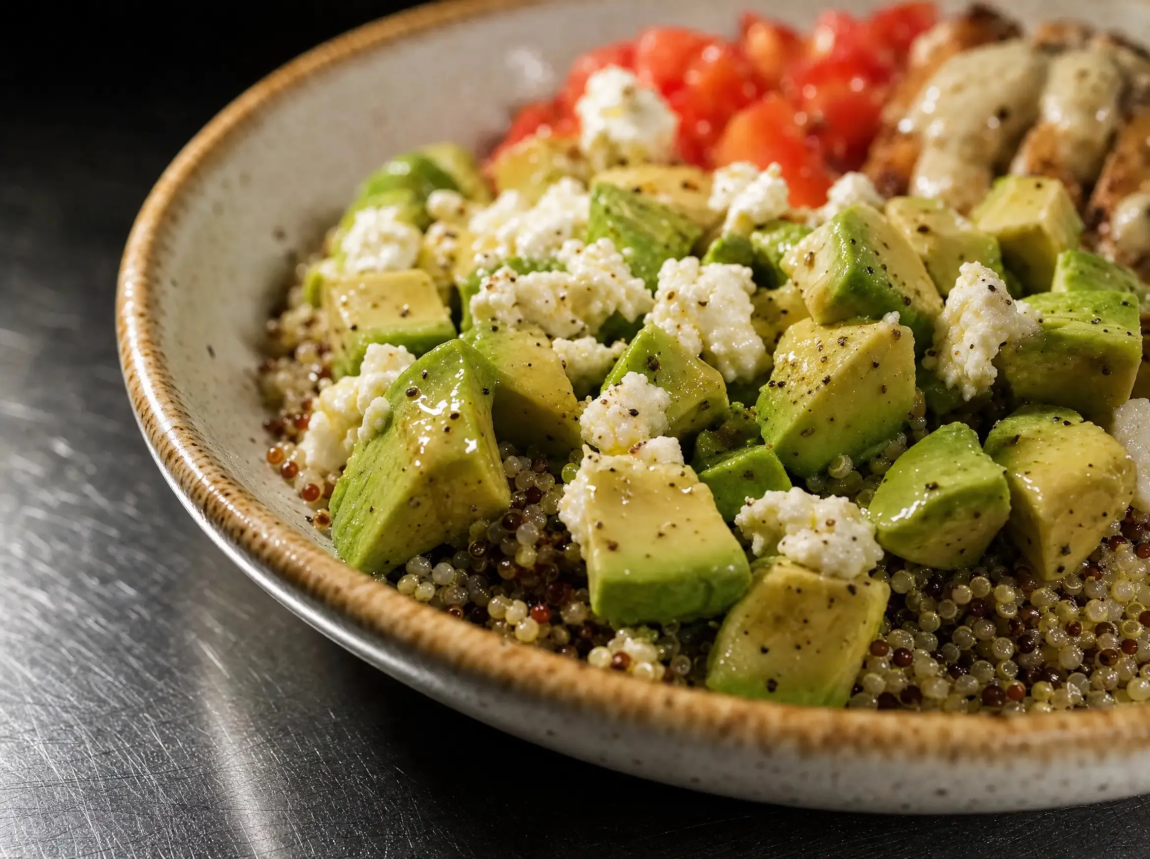Nahaufnahme von gewürfelter Avocado und zerbröckeltem Feta auf dem Quinoa, mit grob gemahlenem schwarzem Pfeffer bestreut.