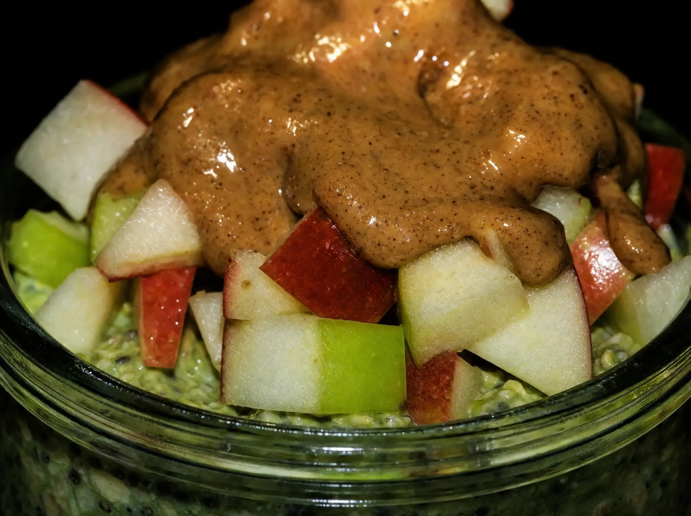 Makroaufnahme von roten und grünen Apfelwürfeln und cremigem Nussmus auf den grünen Matcha Overnight Oats.