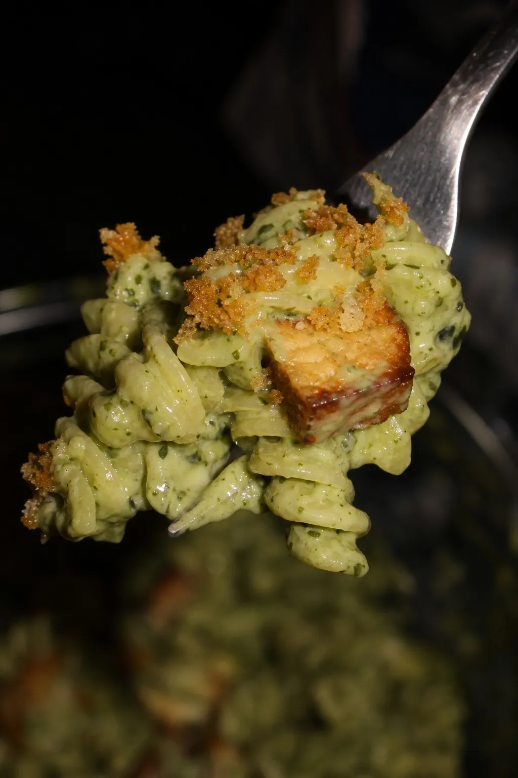 Eine Gabel hebt eine Portion Spinat-Pasta mit Tofu und Panko-Topping aus dem Teller.