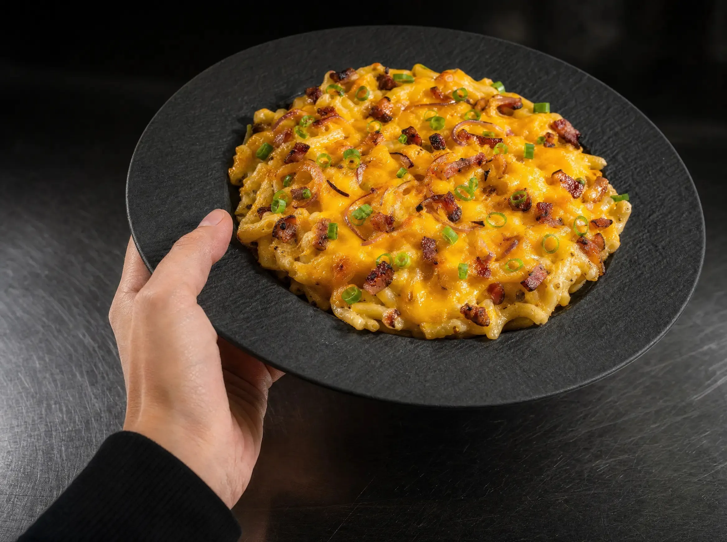 Ein Teller Airfryer Flammkuchenspätzle, in einer Hand gehalten und leicht zur Kamera geneigt.