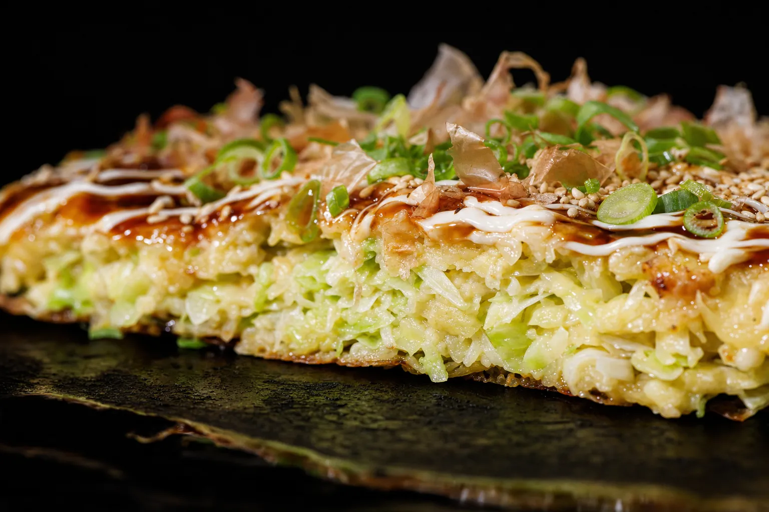 Angeschnittenes Okonomiyaki, im Querschnitt sind der fein gehackte Kohl und der Eierteig zu sehen.