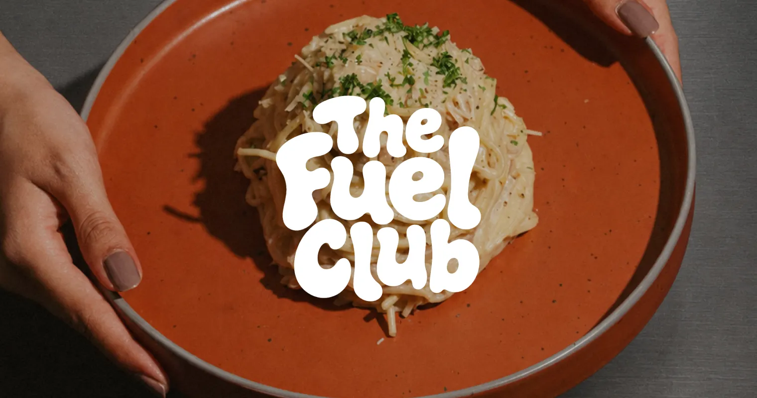 Ein Teller Okonomiyaki wird gehalten, darüber der Schriftzug The Fuel Club