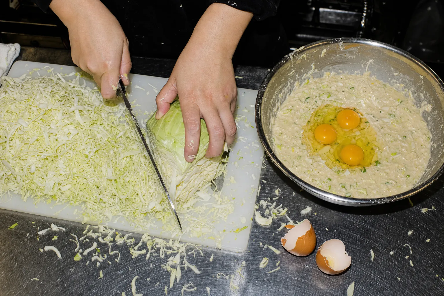 Weißkohl wird auf einem Schneidebrett fein gehackt, daneben eine Schüssel mit Teig und aufgeschlagenen Eiern.